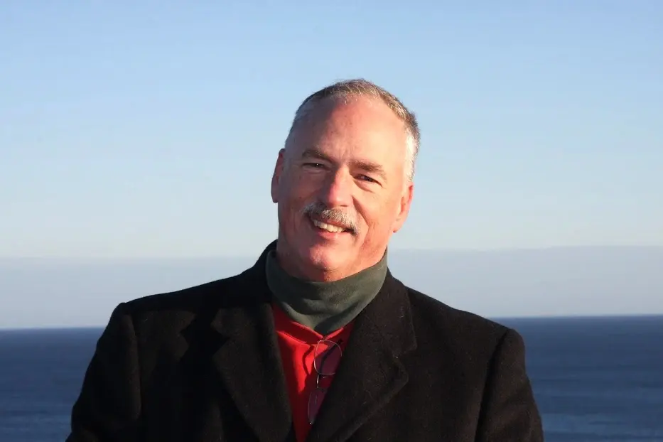 Portrait of Allan Camp in a winter coat, standing above the open ocean on a clear day