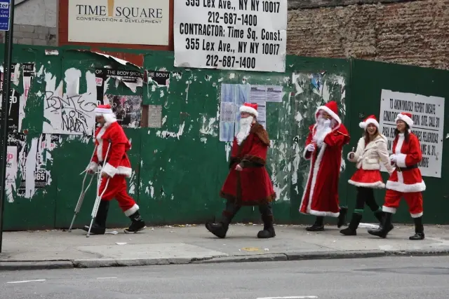 Several people in Santa suits walking a city street past a construction hoarding