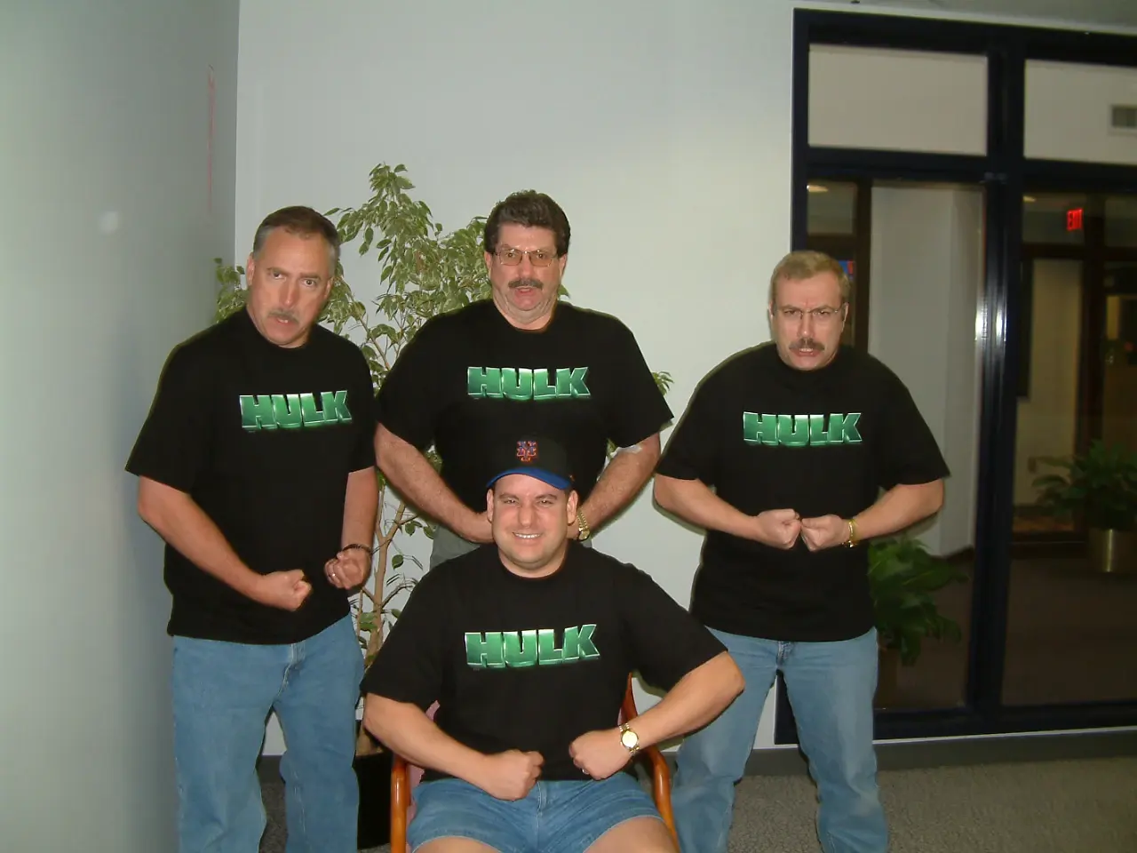 Four men in matching green HULK t-shirts striking bodybuilder poses for the camera