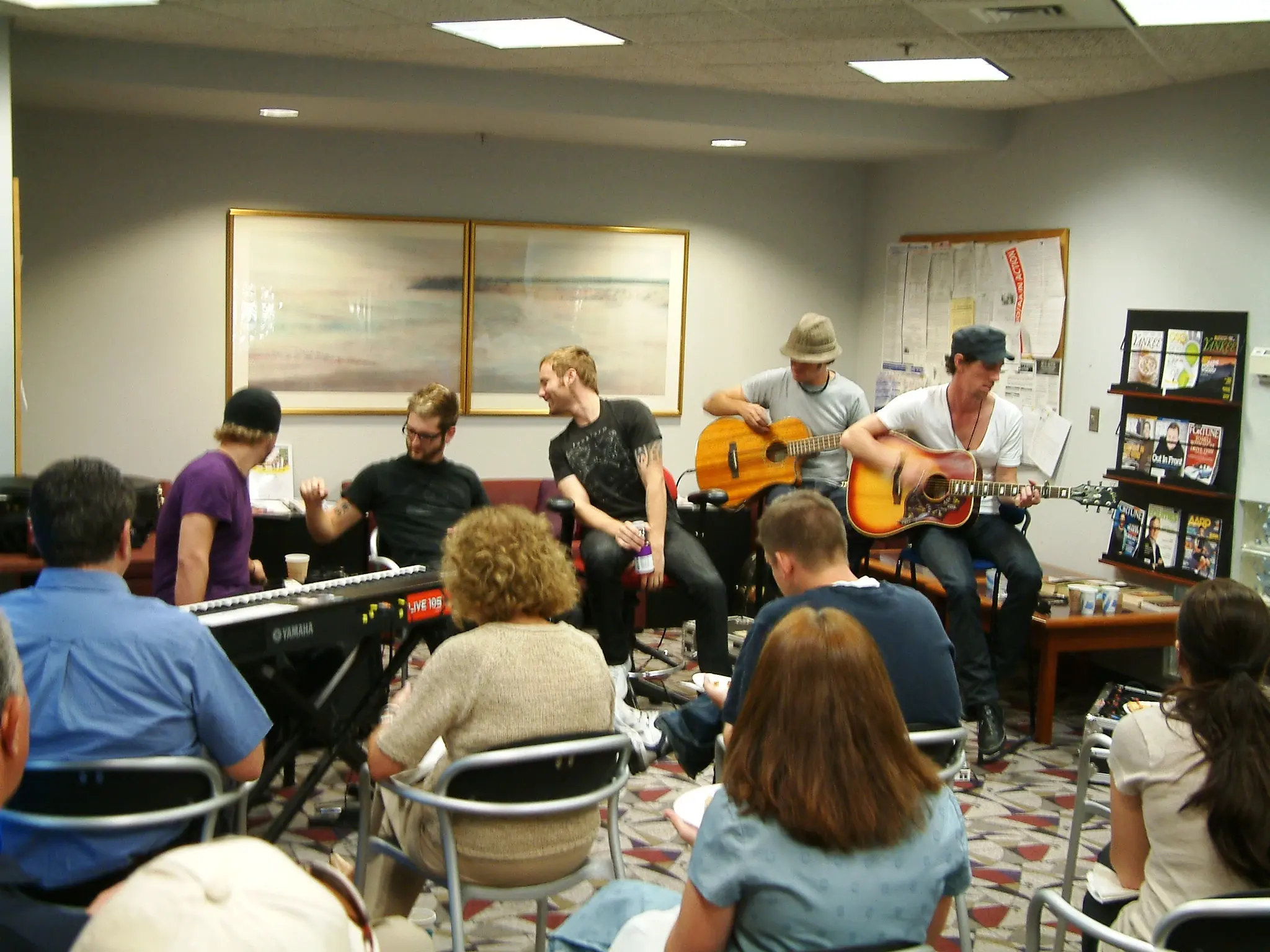 A band playing an acoustic set to a small seated audience in a community room