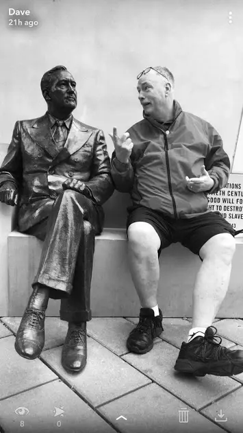 Black and white photograph of a man seated beside a bronze statue of a seated figure, copying its gesture