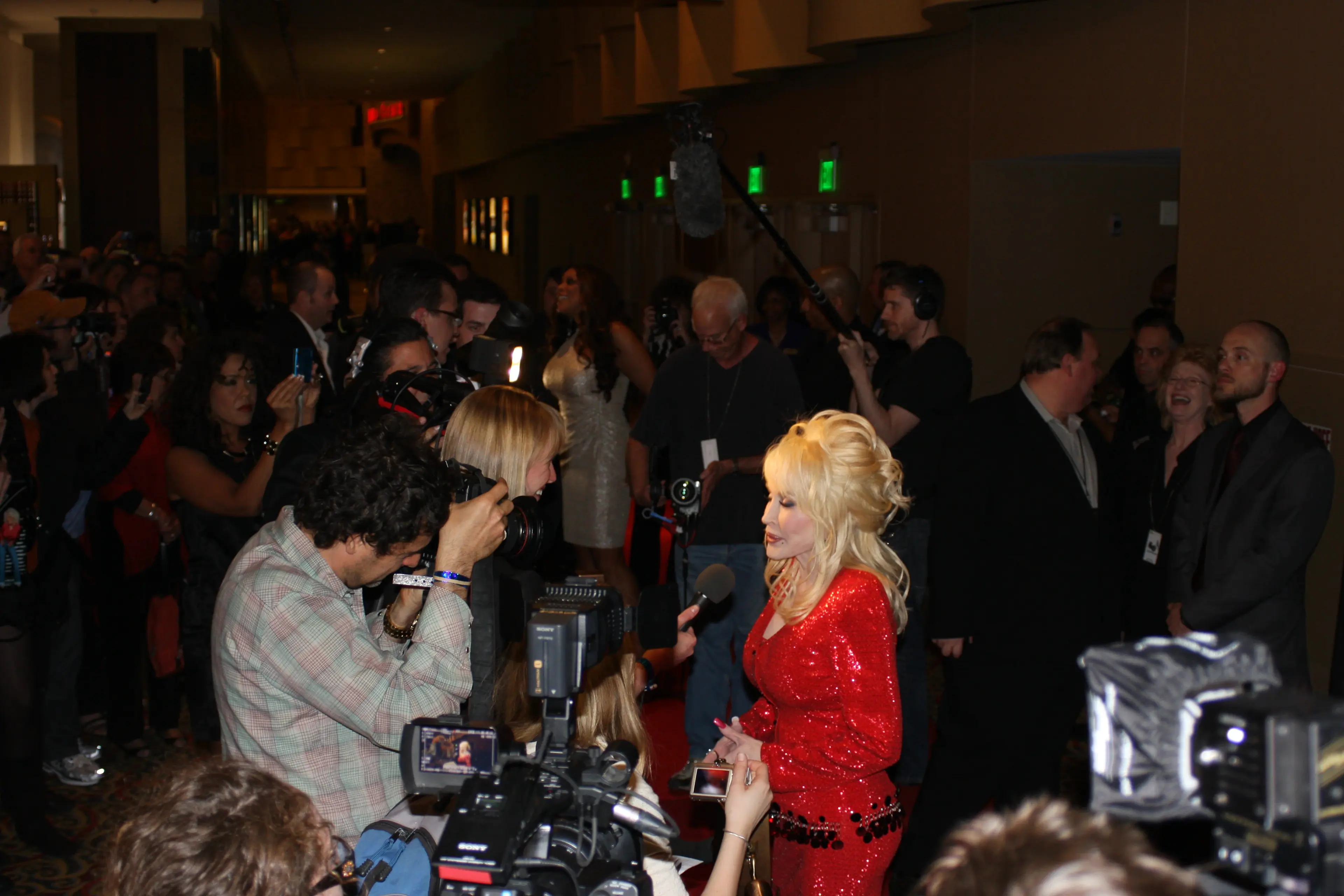 A performer in a red sequinned dress being interviewed on a press line ringed by television cameras
