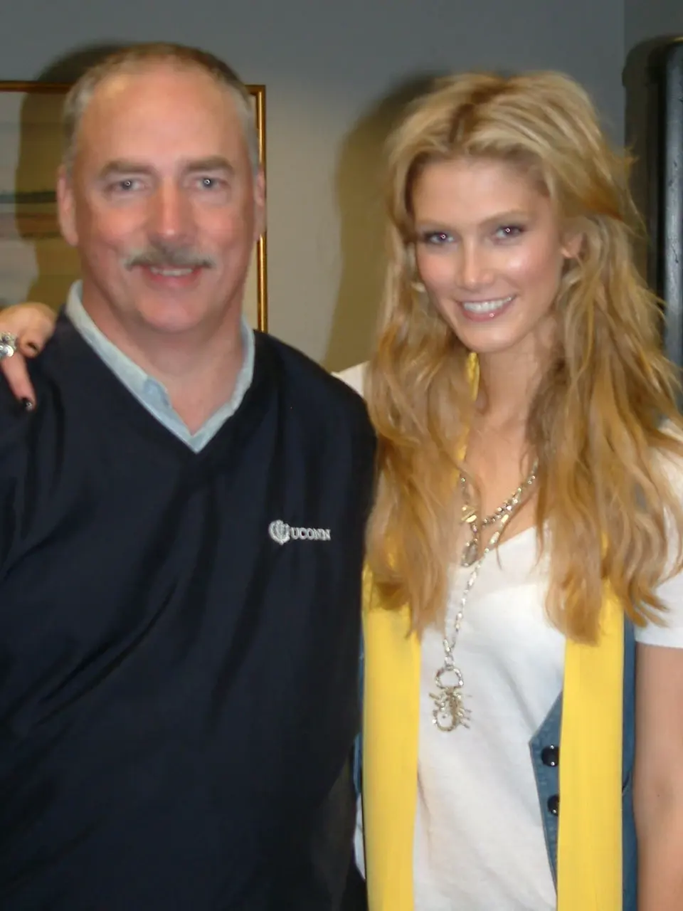A man in a UConn pullover with his arm around a guest wearing a yellow scarf