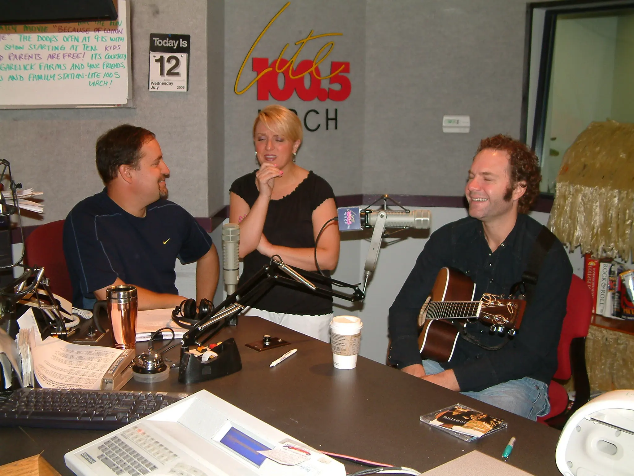 Three people around the WRCH studio table during an in-studio session, one holding an acoustic guitar