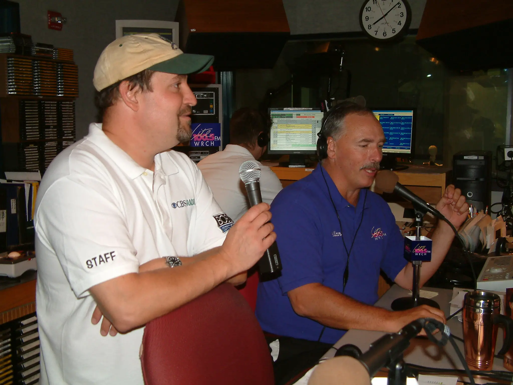 Two men on air in the WRCH studio, one holding a handheld microphone, playout screens behind them