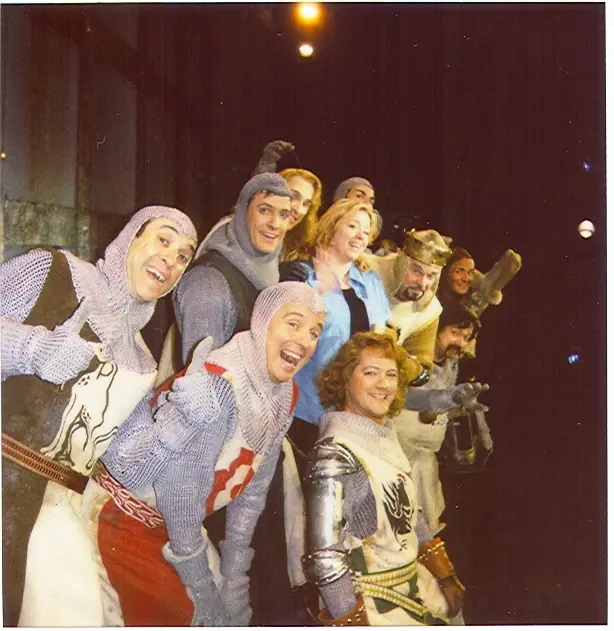 The cast of a stage musical in knight costumes and chainmail crowded together for a curtain-call photograph