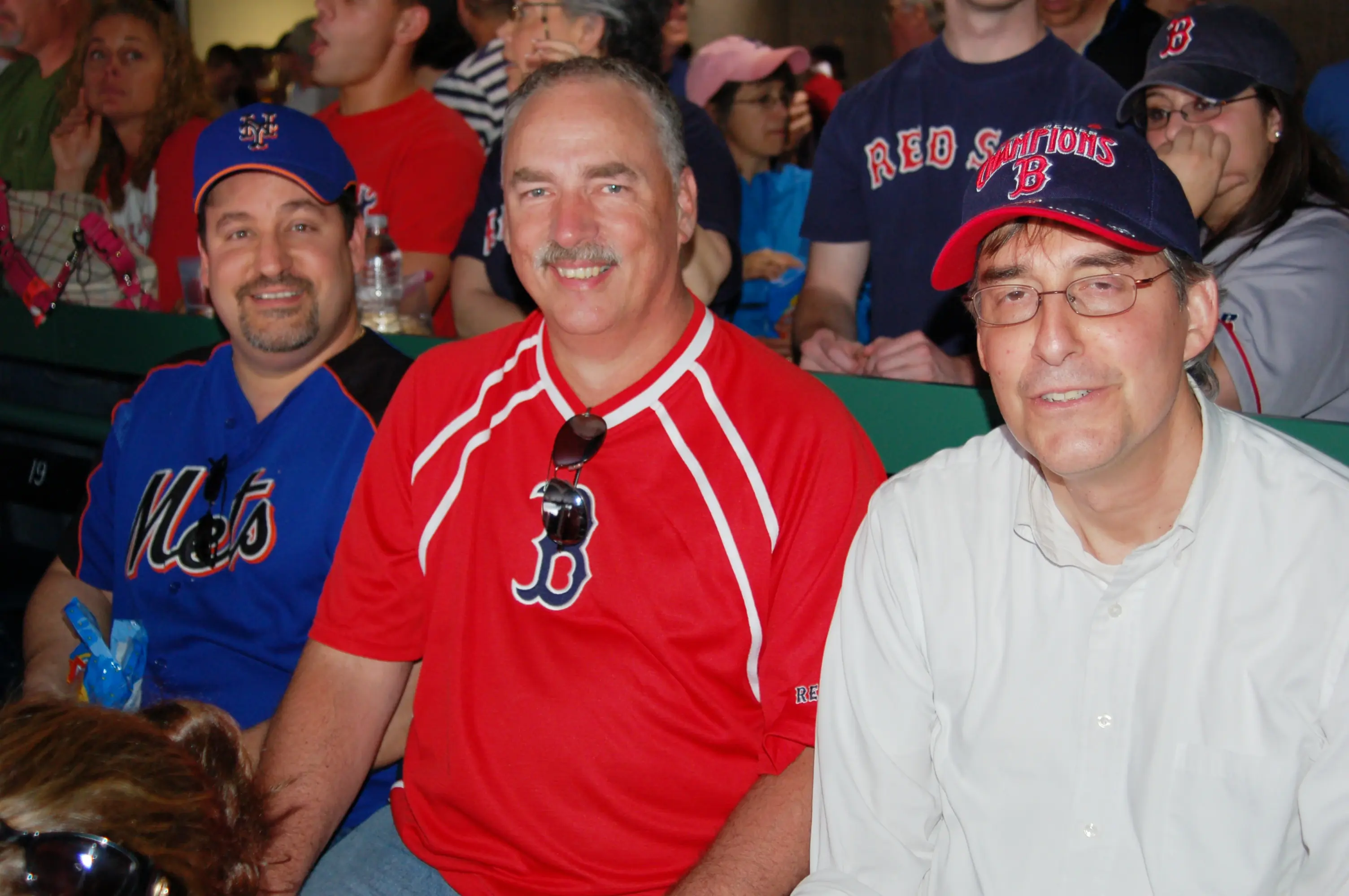 Two men in Red Sox shirts and caps in the stands at a ballgame