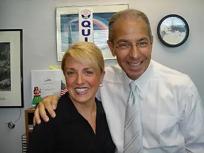 Two colleagues with arms around each other in an office, a rainbow poster on the wall behind them