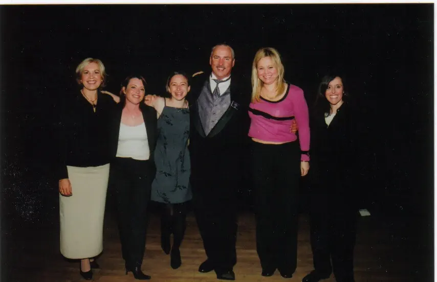Five people posed together for a group portrait on a darkened stage