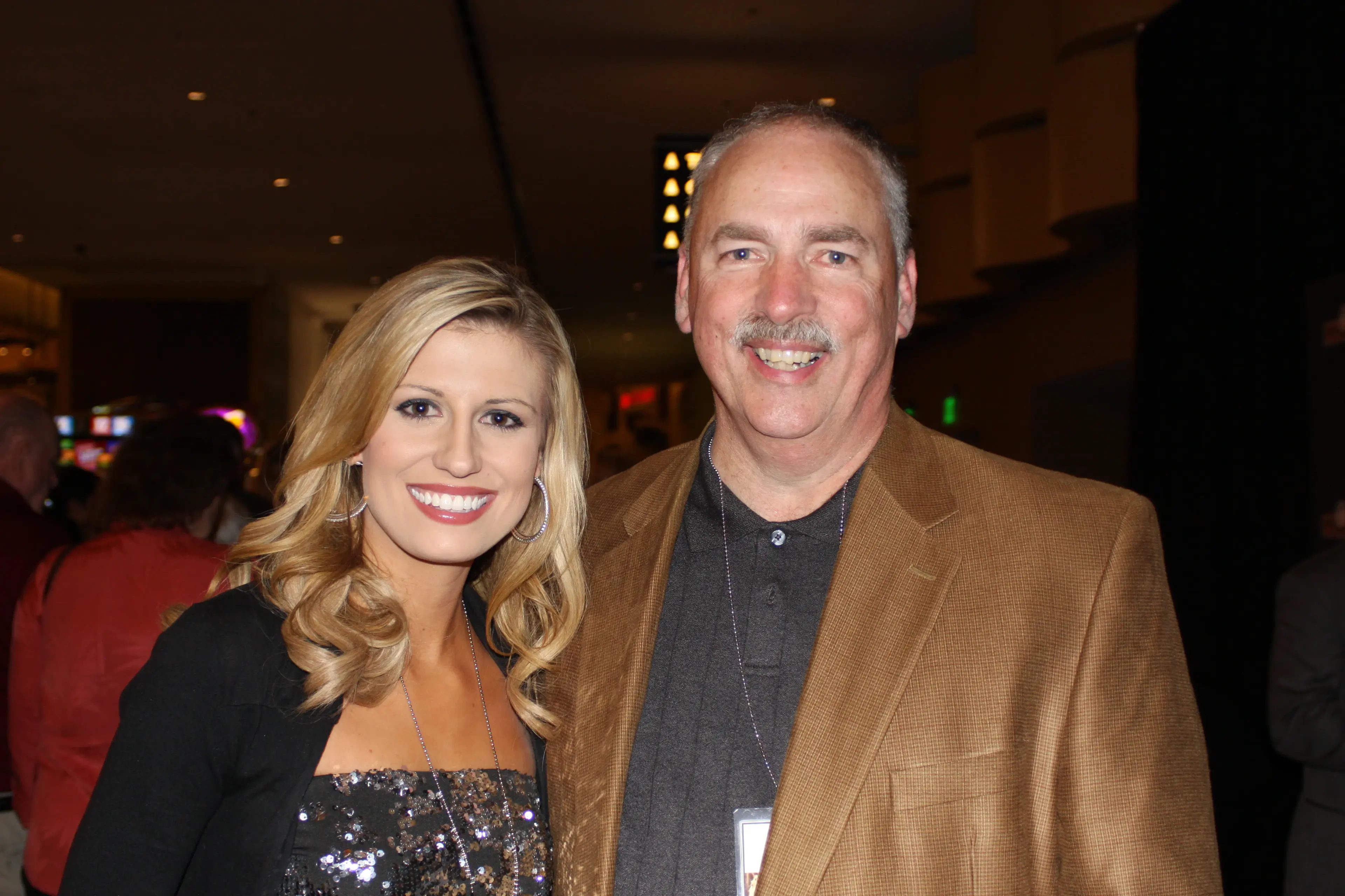 A guest in a sequinned top photographed with a man in a tan jacket at an evening event