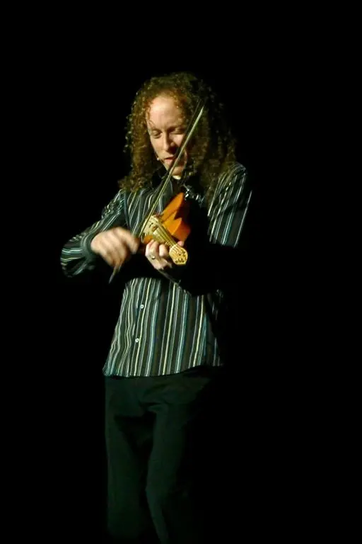 A violinist in a striped jacket performing under a spotlight on an otherwise dark stage