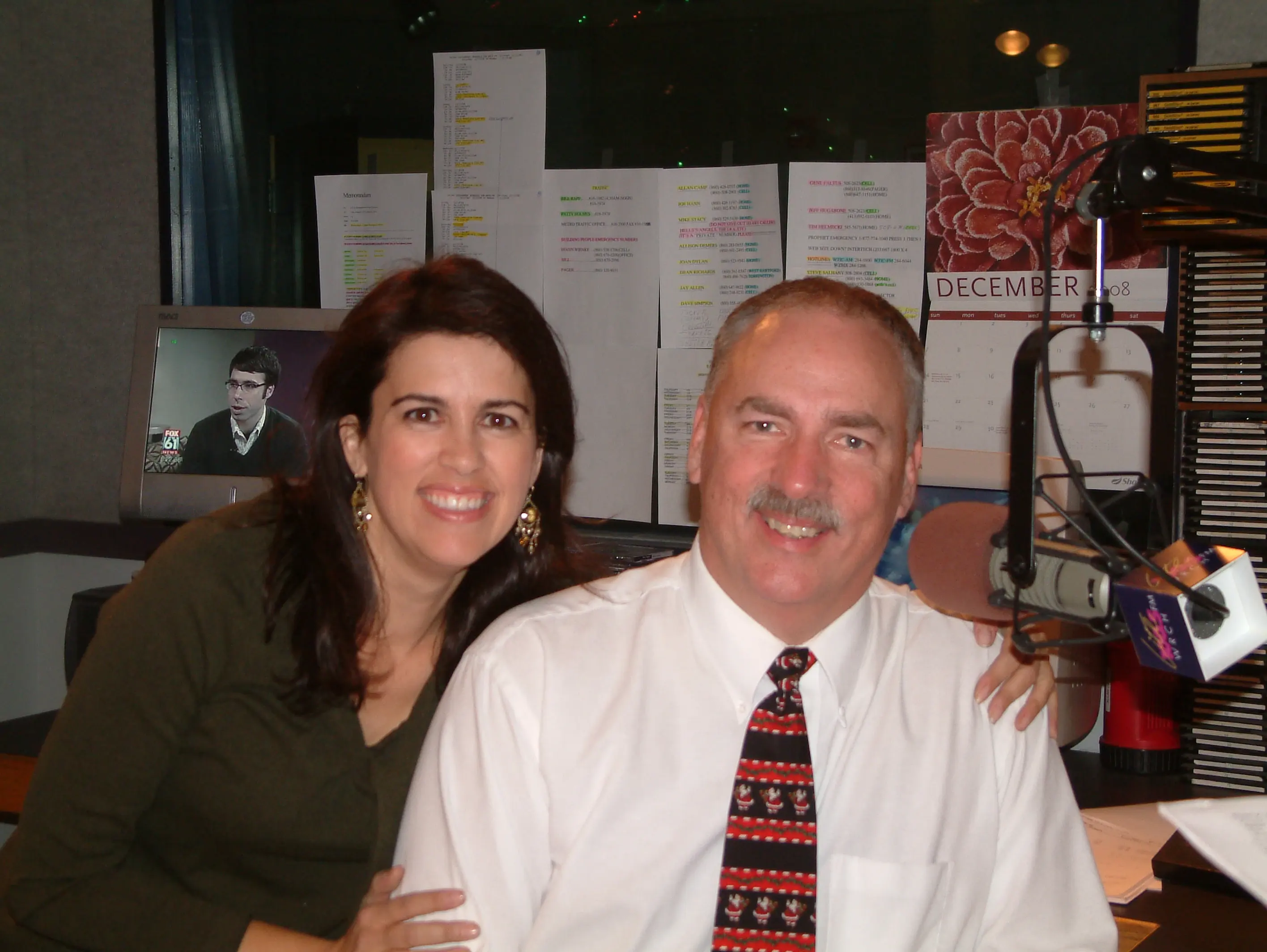 Two people in the WRCH studio at Christmas, one wearing a holiday tie, a December calendar on the wall behind