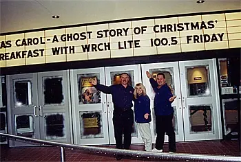 Three people in station jackets under a theatre marquee reading A GHOST STORY OF CHRISTMAS WITH WRCH LITE 100.5 FRIDAY