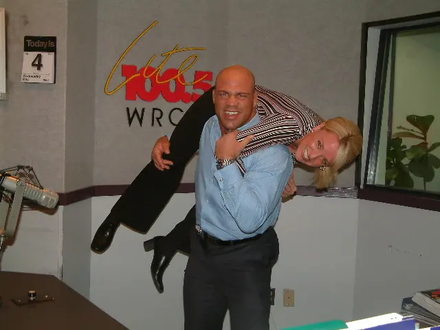 A man carrying a colleague over his shoulder for a joke photograph beneath the Lite 100.5 WRCH wall logo