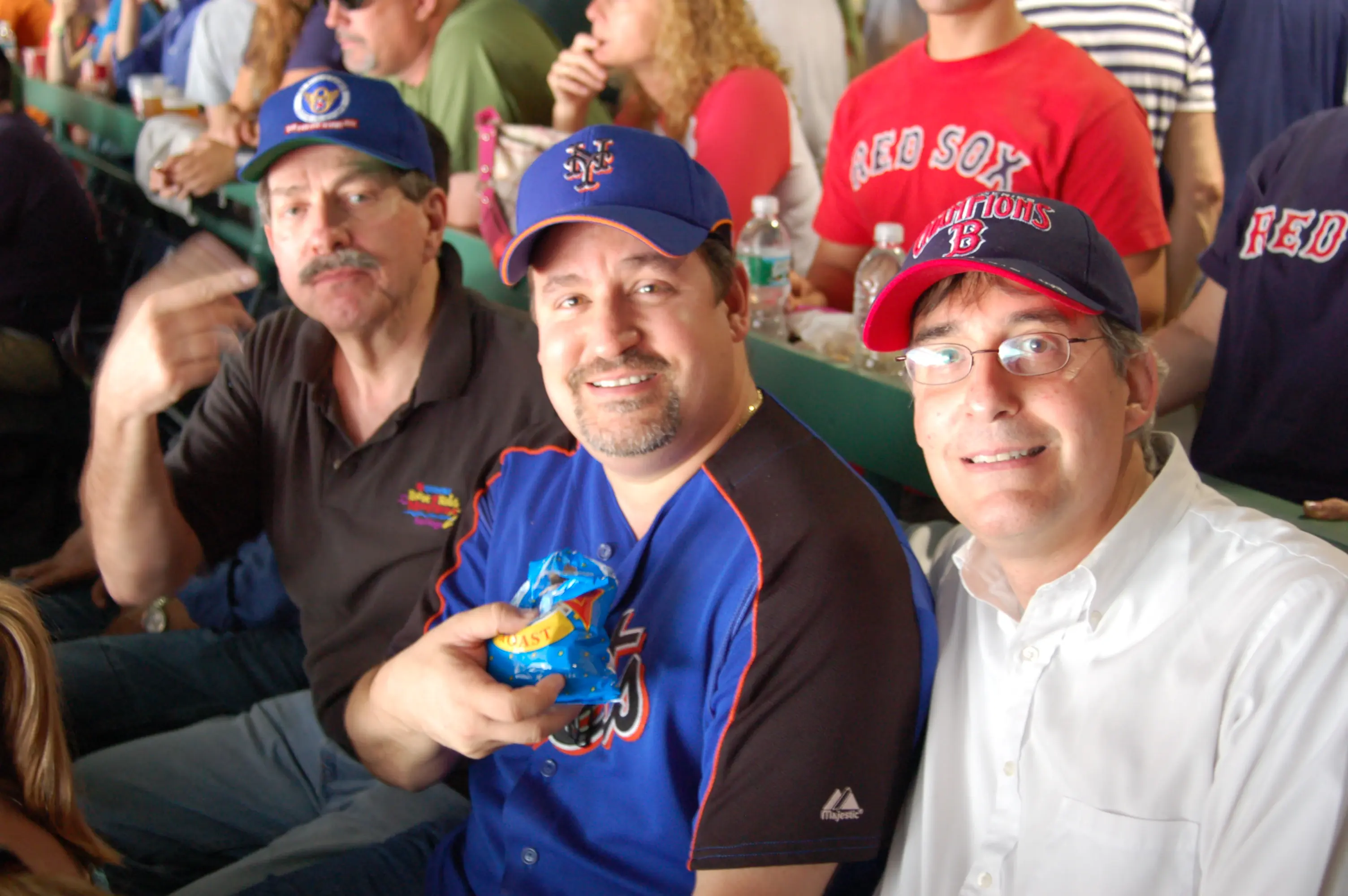 Three men in baseball caps and team shirts seated together at a ballgame