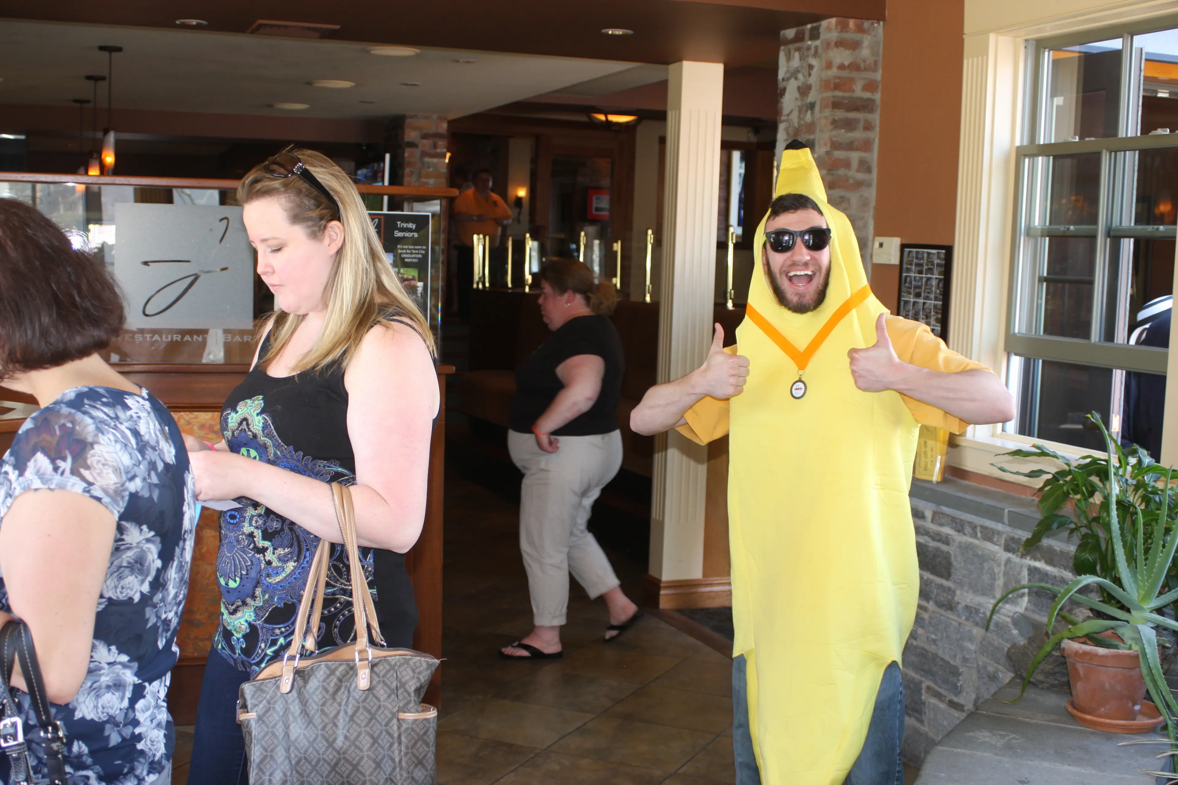 Someone in a banana costume giving a thumbs up in a restaurant lobby while guests queue in the foreground