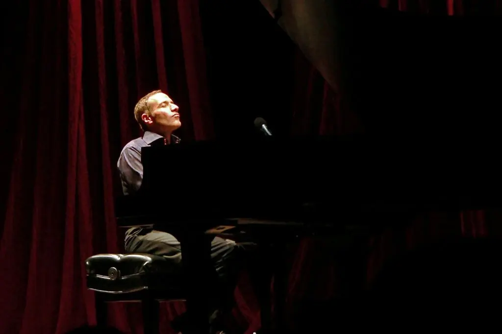 A pianist at a grand piano on a dark stage, red curtains drawn behind him