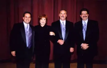 Three people in formal wear posed together in front of a red stage curtain