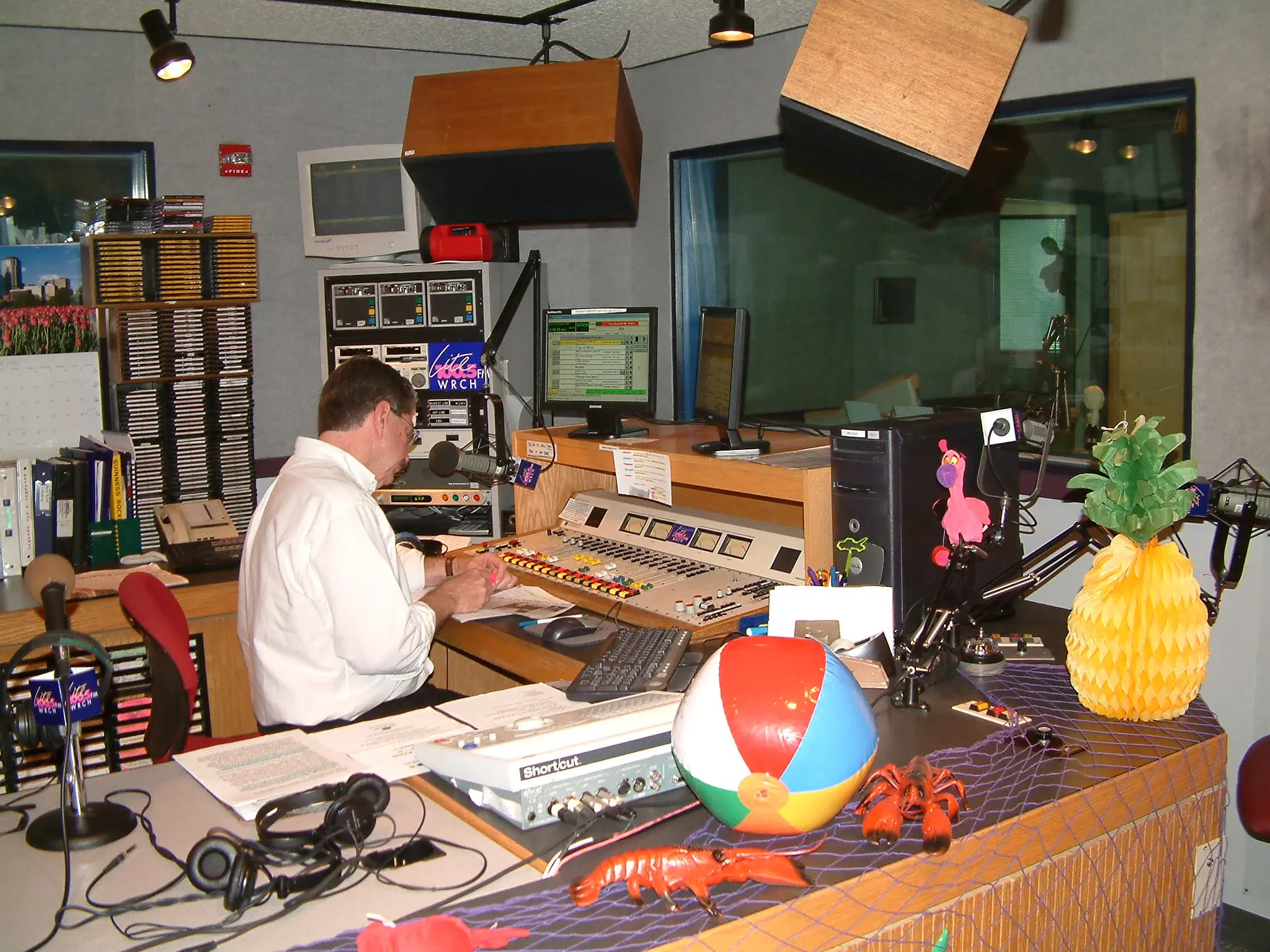 The WRCH on-air studio seen from behind the presenter at the board, CD racks on the wall and a beach ball and toy lobster on the desk
